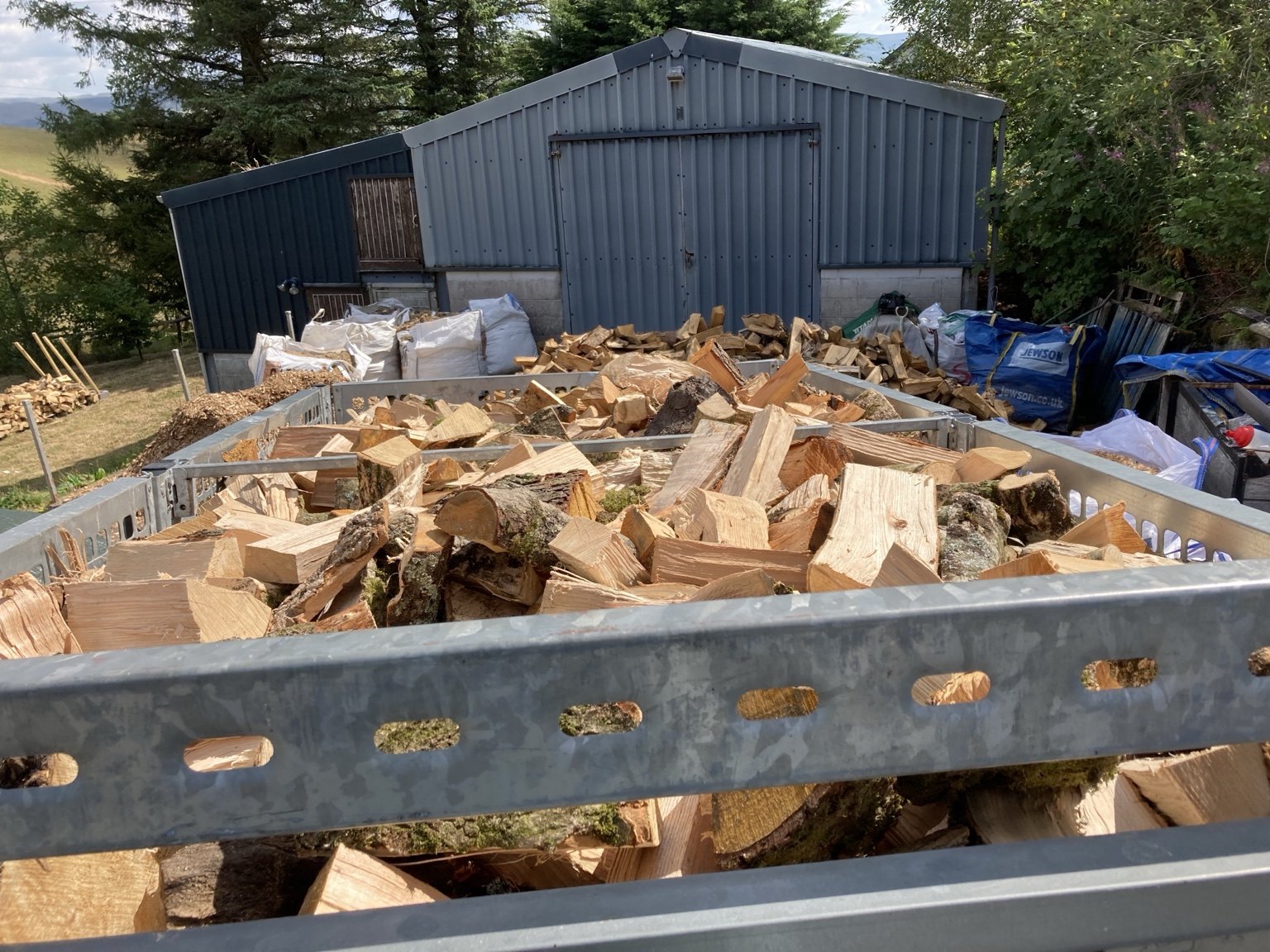 Live With Nature firewood processing area with split logs and bulk handling.